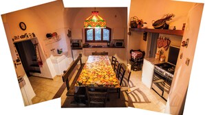 A kitchen with a dining table covered with a fruit pattern tablecloth, a stove, and a window with decorative iron bars. - Holiday in a comfortable and renovated ancient villa (mottola)