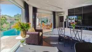 A modern hotel room with a balcony, large windows, a dining area, and a TV. - Cascade House,  Luxury Vila in Carvoeiro (Carvoeiro)