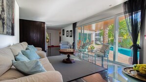 A modern living room with a sofa, a glass coffee table, and a view of an outdoor pool area. - Cascade House,  Luxury Vila in Carvoeiro (Carvoeiro)