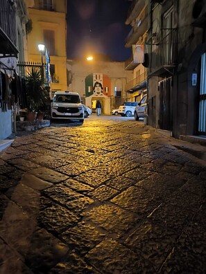 A cobblestone street at night with a white car parked on the left and a person walking towards a building with a mural.