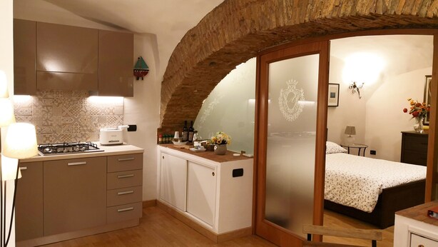 A compact room with a kitchen, a bed with a floral bedspread, and a small table. - L' Arcata a Montesanto 1700s courtyard, metro & funicular (Napoli)