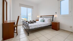 Een slaapkamer met een bed, een bureau, een stoel, een nachtkastje, een plafondventilator en een raam.