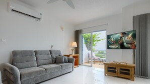 Een moderne woonkamer met een grijze bank, een houten tv-meubel en een grote flatscreen-televisie waarop een film poster staat.