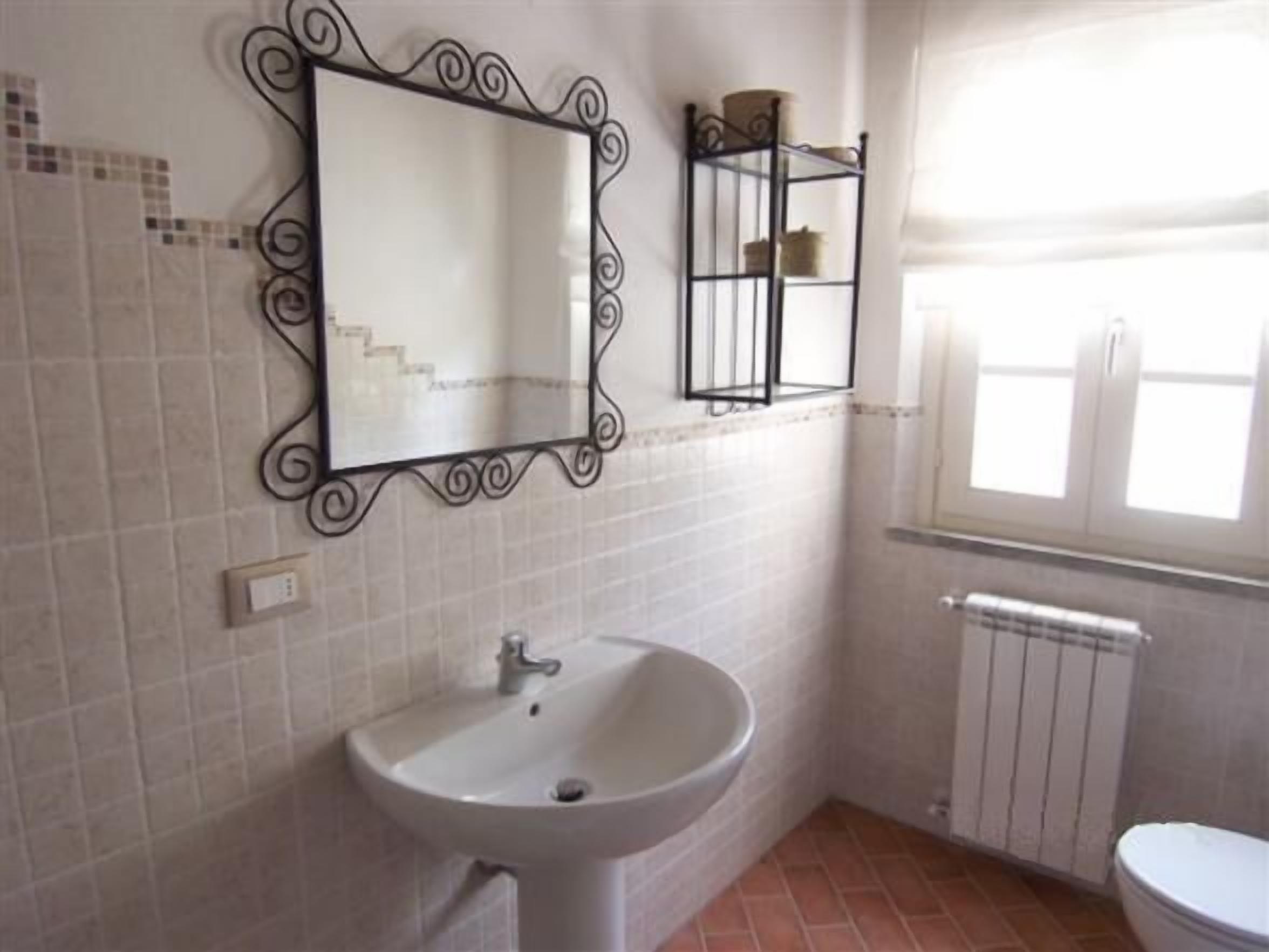 A bathroom with a white sink, a mirror with a decorative frame, a window, and a radiator.