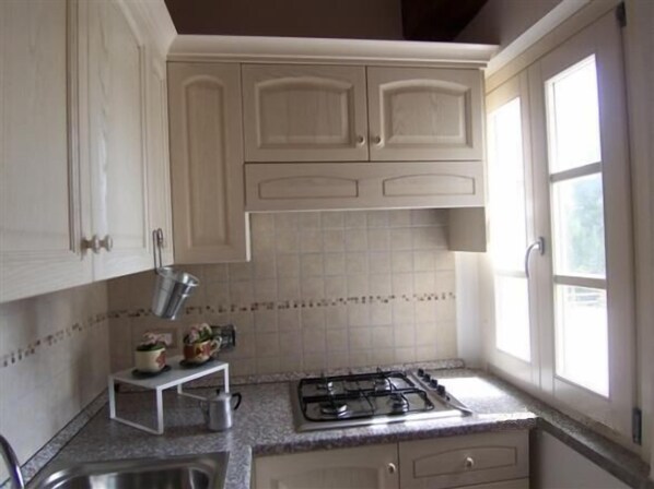 A kitchen with white cabinets, a gas stove, a small countertop, and a window.