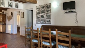 A dining area with wooden chairs and a bench, a wall with framed pictures, a television mounted on the wall, and a radiator on the wall. - Villetta dei lecci - Charming detached cottage (Monteverdi Marittimo)