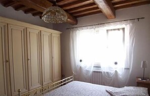 Een slaapkamer met een grote garderobe, een bed met een witte dekbedovertrek, een hanglamp en een raam met dunne gordijnen.