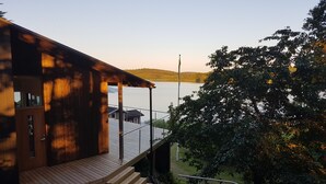 Una cabaña de madera con terraza, con vista a un lago rodeado de árboles.