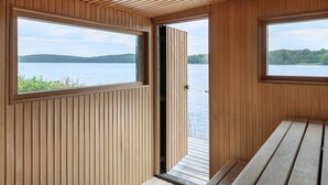 Una cabaña con paredes de madera y un banco, con amplias ventanas que dan a un lago.