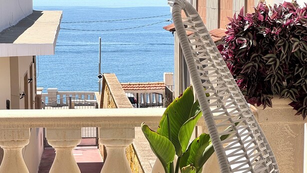 A balcony with a hanging chair, a potted plant, and a view of the sea. - B&B Santa Maria di Leuca (Castrignano del Capo)