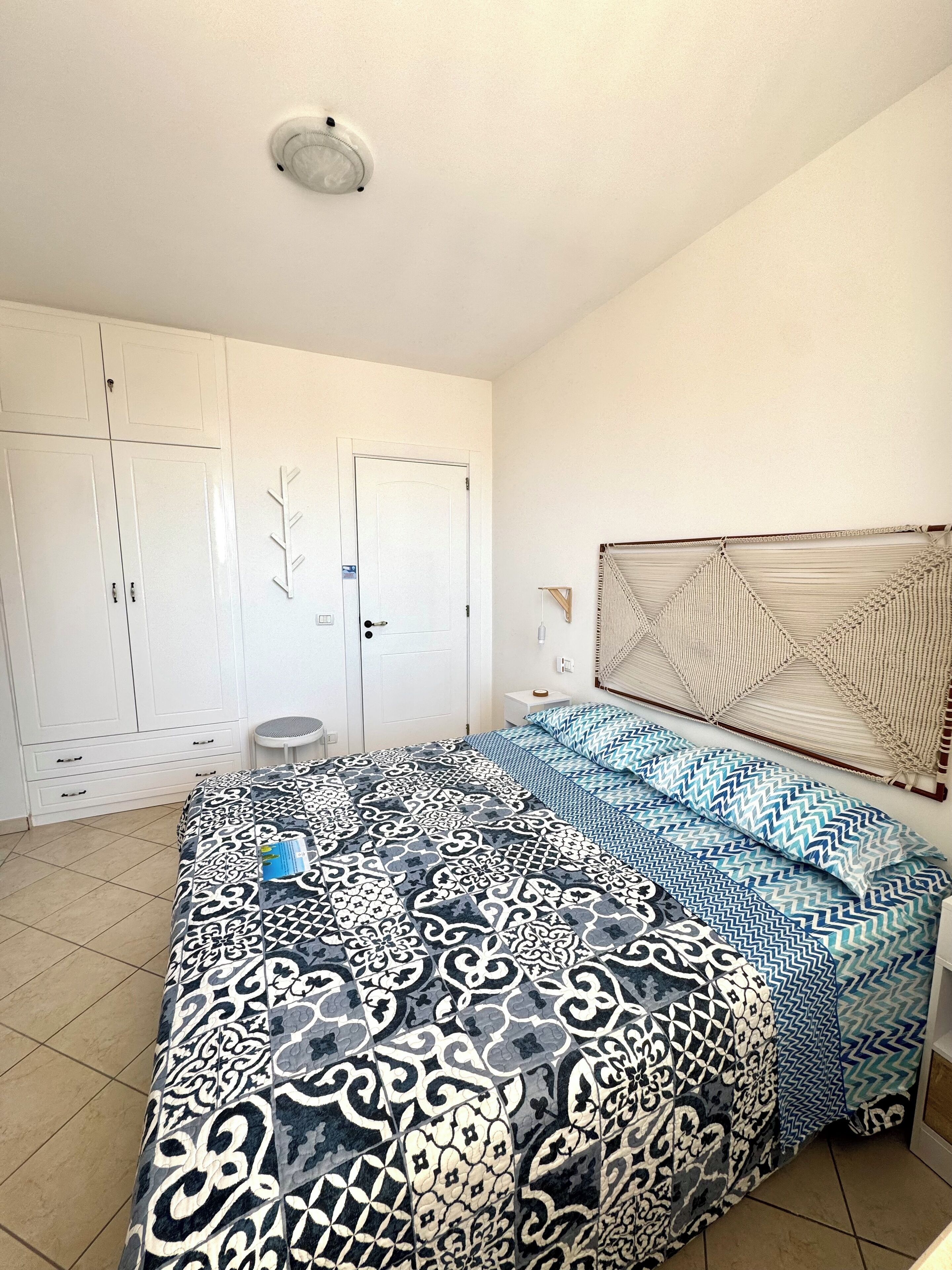 Une chambre à coucher avec une couvre-lit à motifs, une tête de lit, une armoire et un luminaire au plafond.