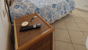 A bedroom with a bed, a bedside table with a remote control, a hanging light fixture, a wardrobe, and a view of the outside. - B&B Santa Maria di Leuca (Castrignano del Capo)