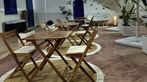 A dining area with wooden tables and chairs, a large umbrella overhead, and a stone wall in the background. - B&B Santa Maria di Leuca (Castrignano del Capo)