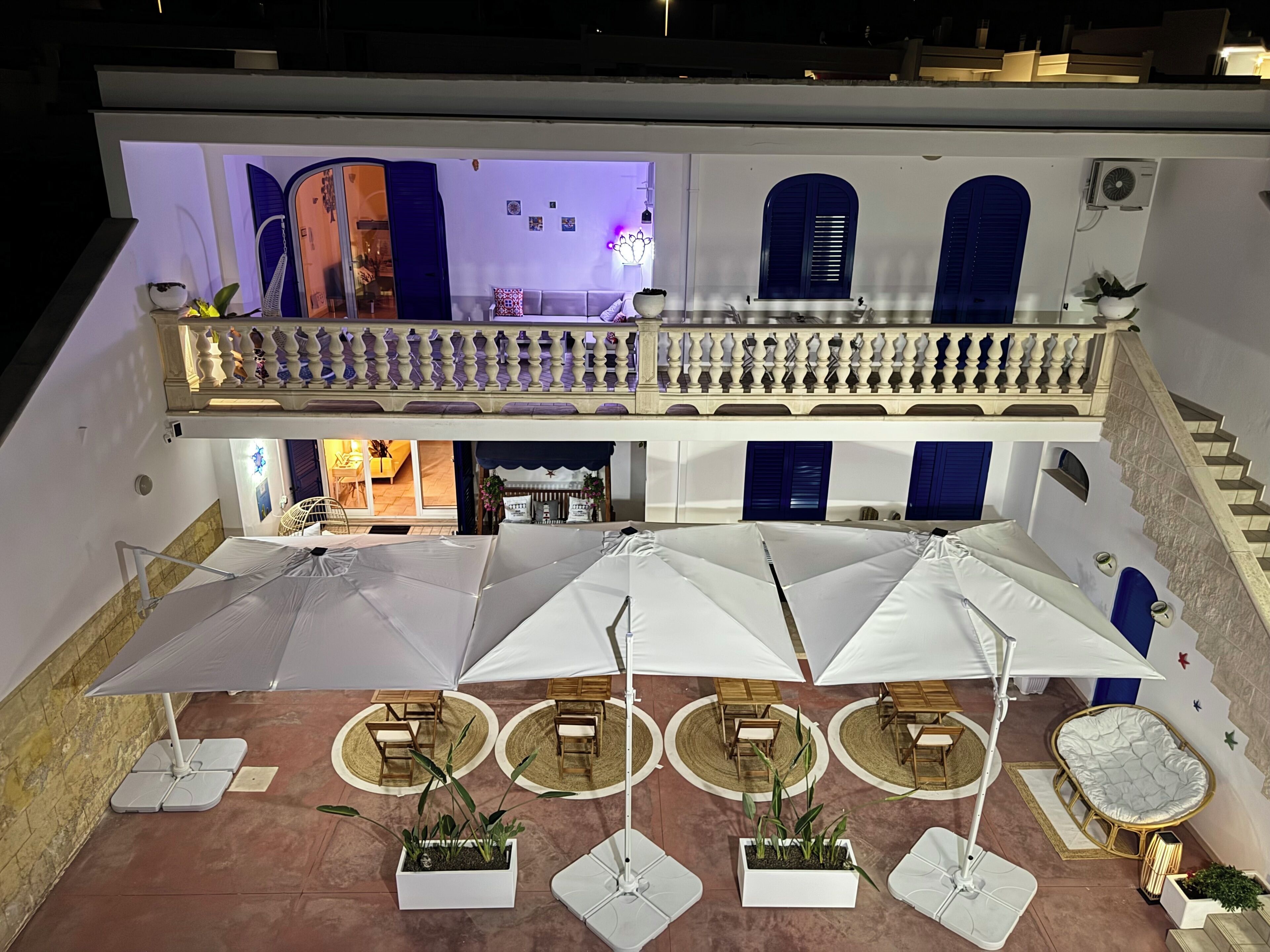 A hotel courtyard with outdoor seating, a balcony, and a staircase.