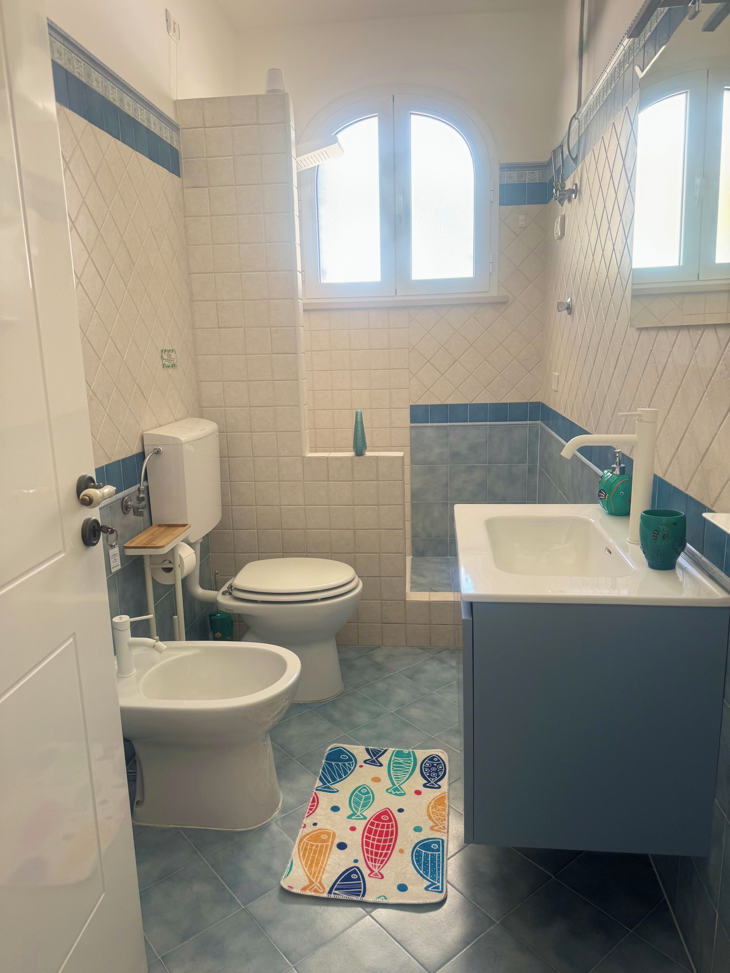 Et badeværelse med toilet, bidet, vask og et vindue.