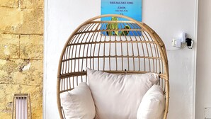 A wicker chair with white cushions, a wall clock, a decorative snowflake, and a sign indicating breakfast time. - B&B Santa Maria di Leuca (Castrignano del Capo)