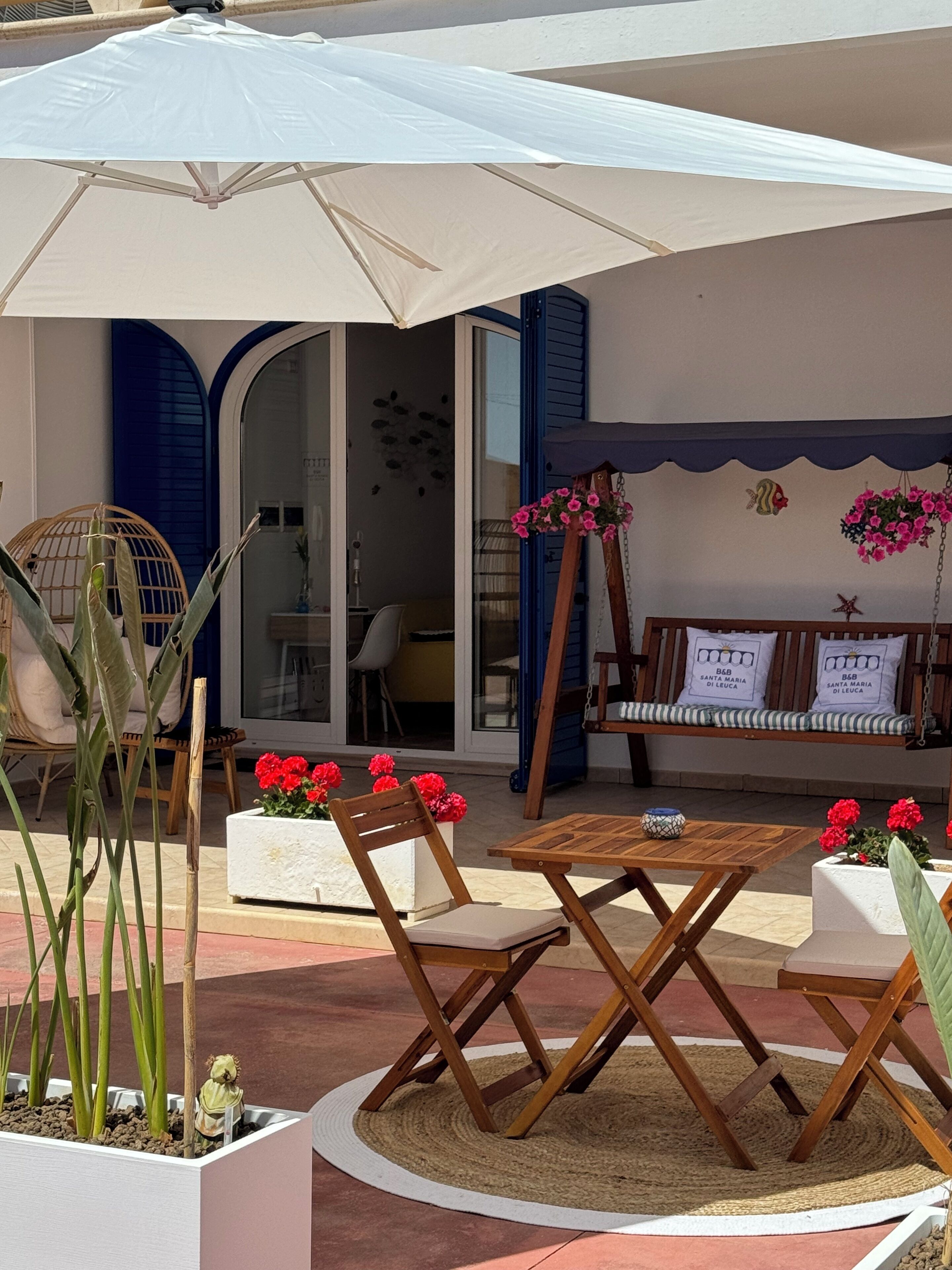 An outdoor seating area with a table and chairs, a swing, and potted plants.