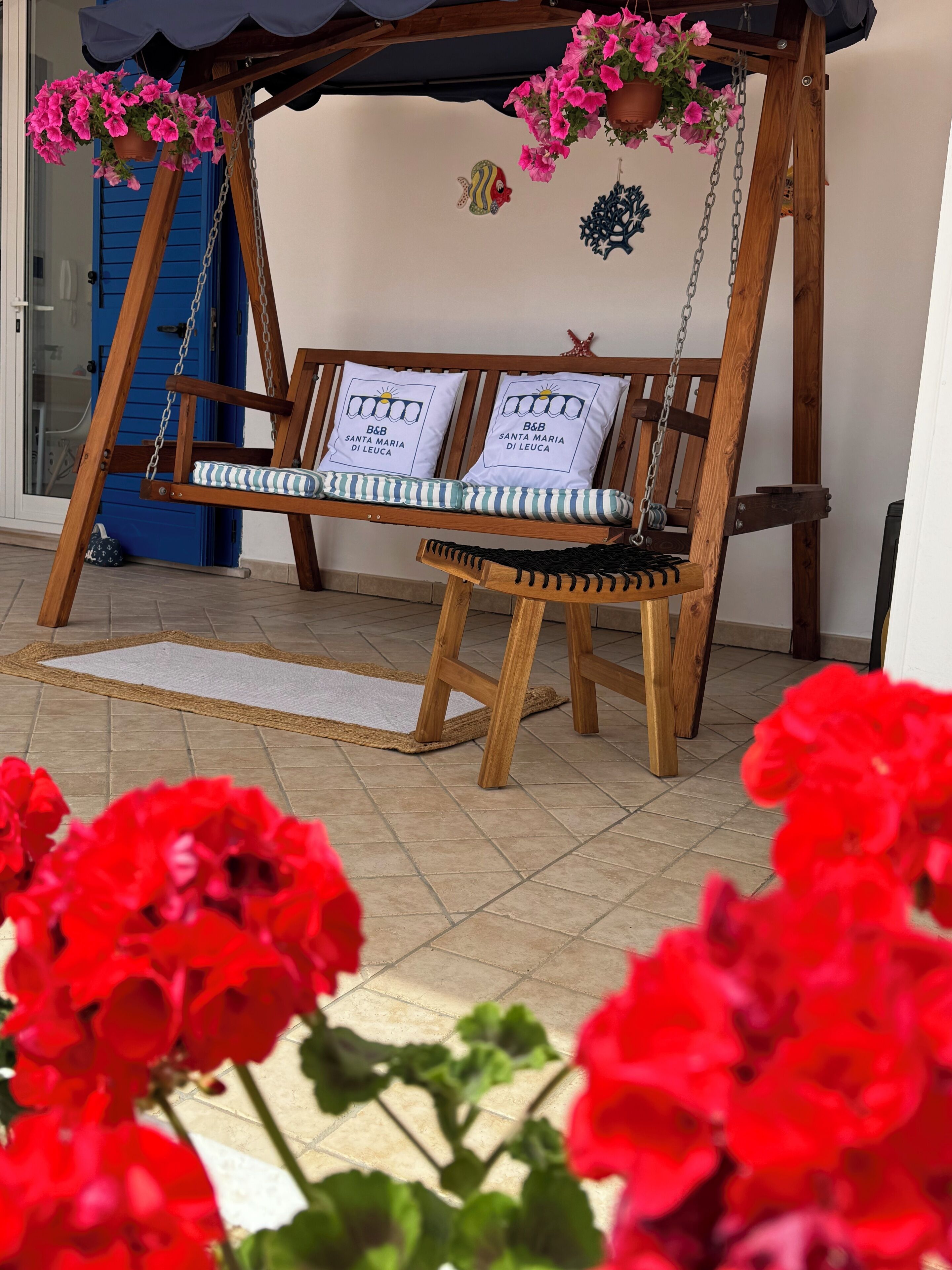 Una hamaca de madera con cojines blancos y una puerta azul al fondo.
