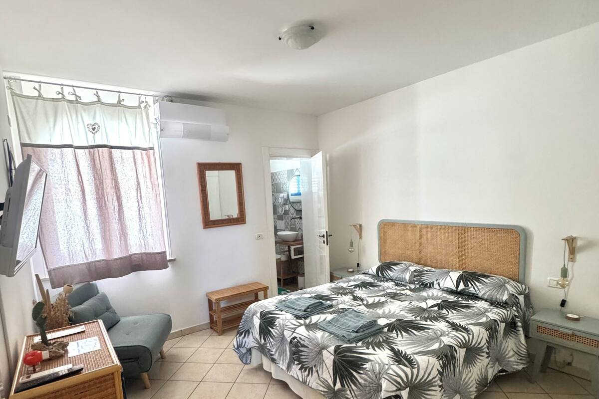 A bedroom with a bed, a desk, a chair, a television, and a bathroom visible through an open door.