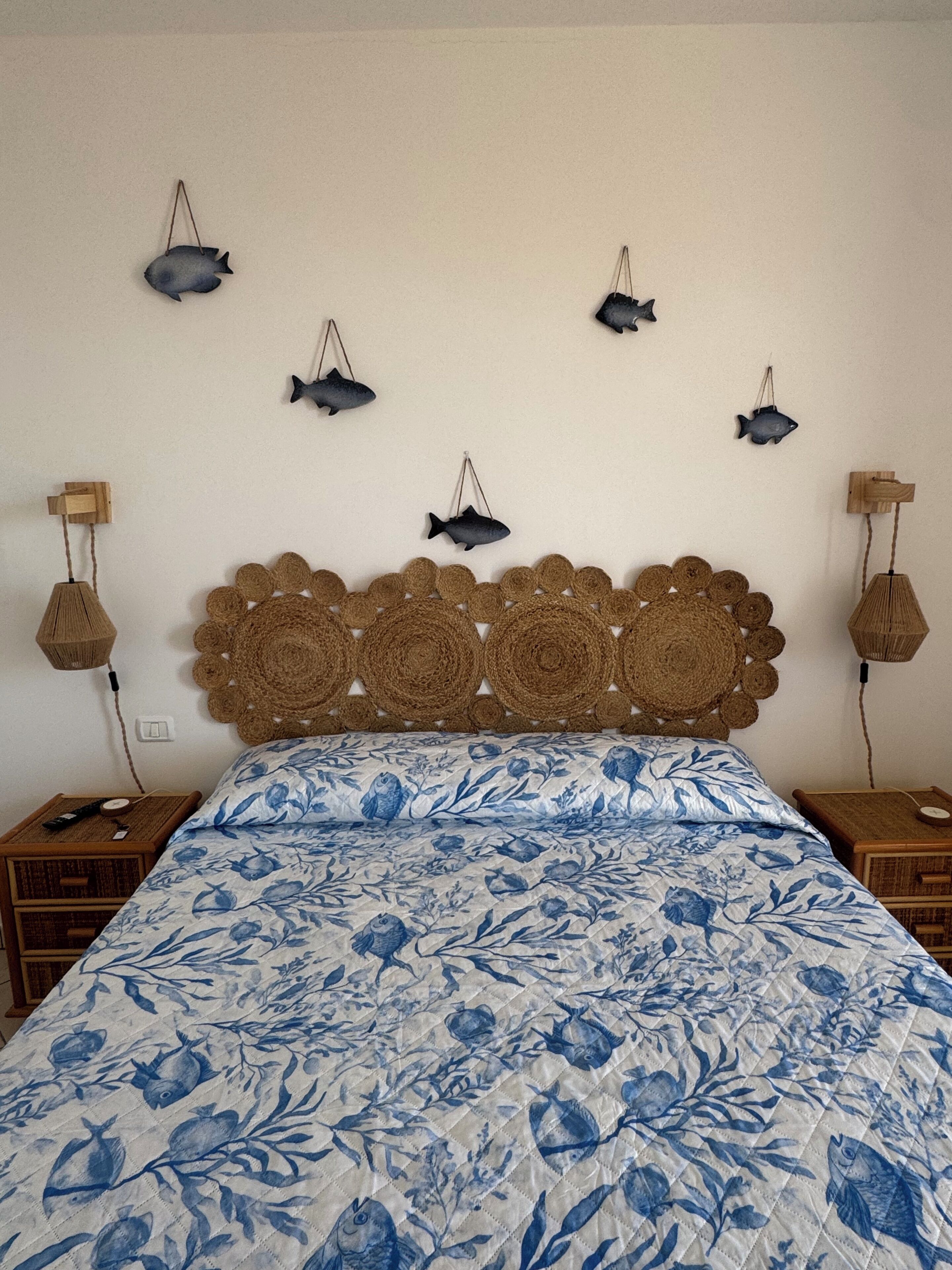Un lit recouvert d’une couvre-lit à motifs floraux bleus, avec une tête de lit en osier et des décorations murales représentant des poissons.