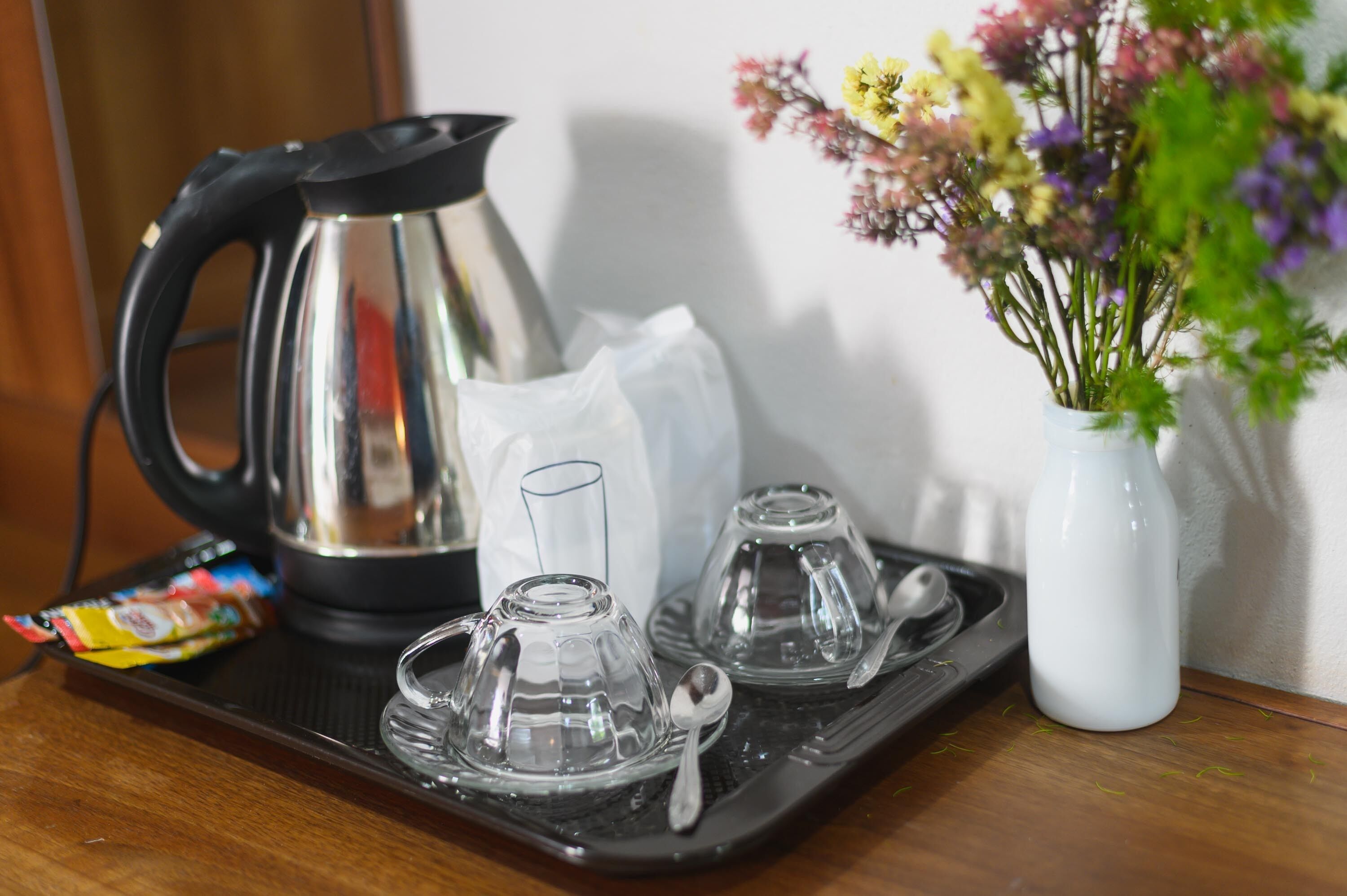 Un plateau avec une bouilloire, des verres, un vase avec des fleurs et un paquet de collations.