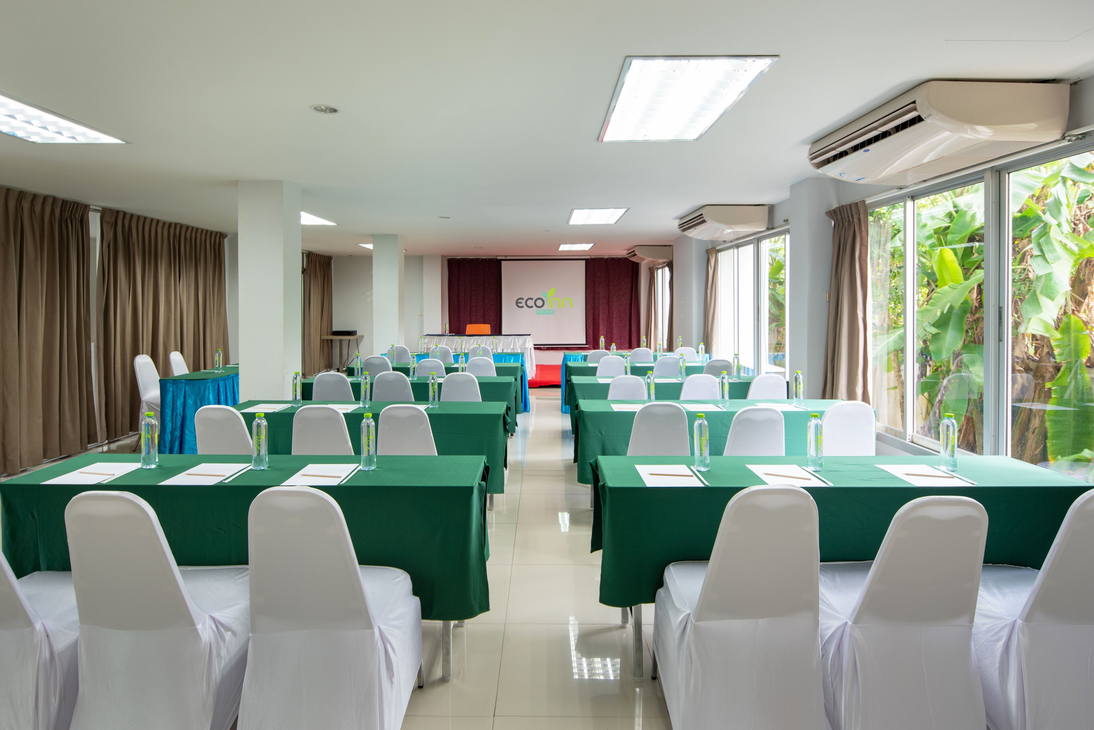 Un salón de conferencias con filas de mesas y sillas, un atril y una pantalla para presentaciones.
