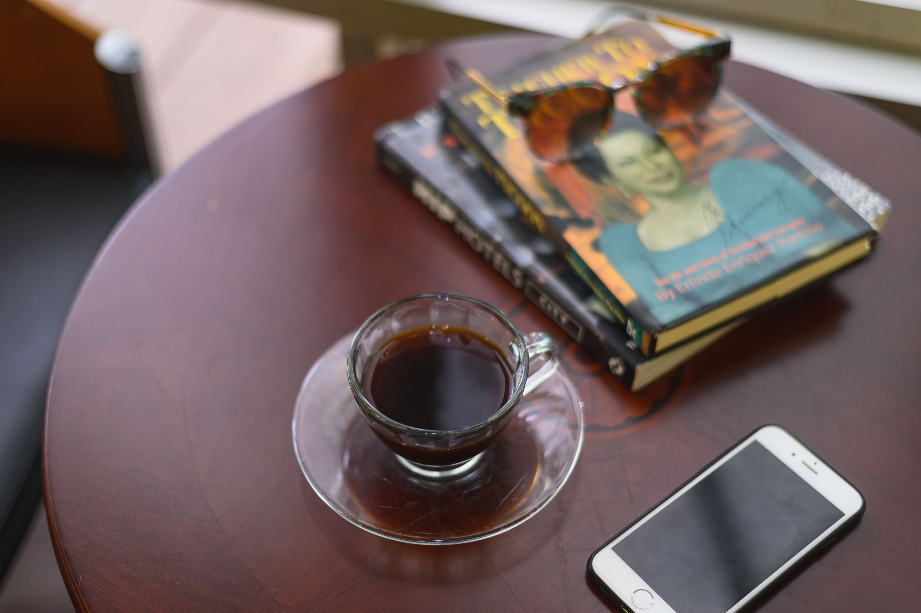 Eine Tasse Kaffee auf einem Untertasse, ein Smartphone und ein Bücherstapel auf einem runden Tisch.