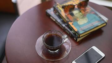 Una tazza di caffè su un piattino, uno smartphone e una pila di libri su un tavolo rotondo.