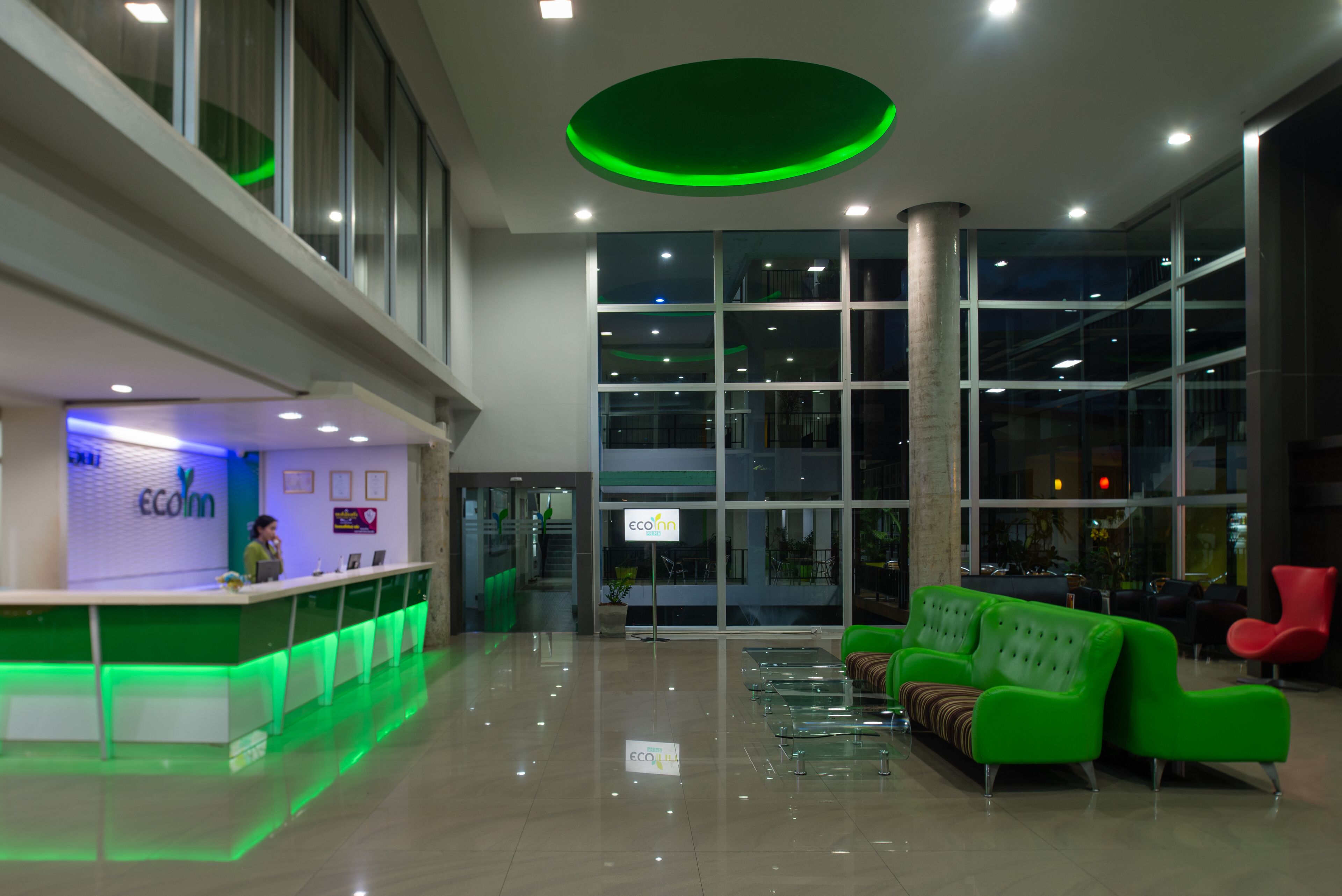 A modern lobby with a reception desk, green seating area, and large windows.