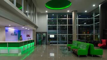 A modern lobby with a reception desk, green seating area, and large windows.