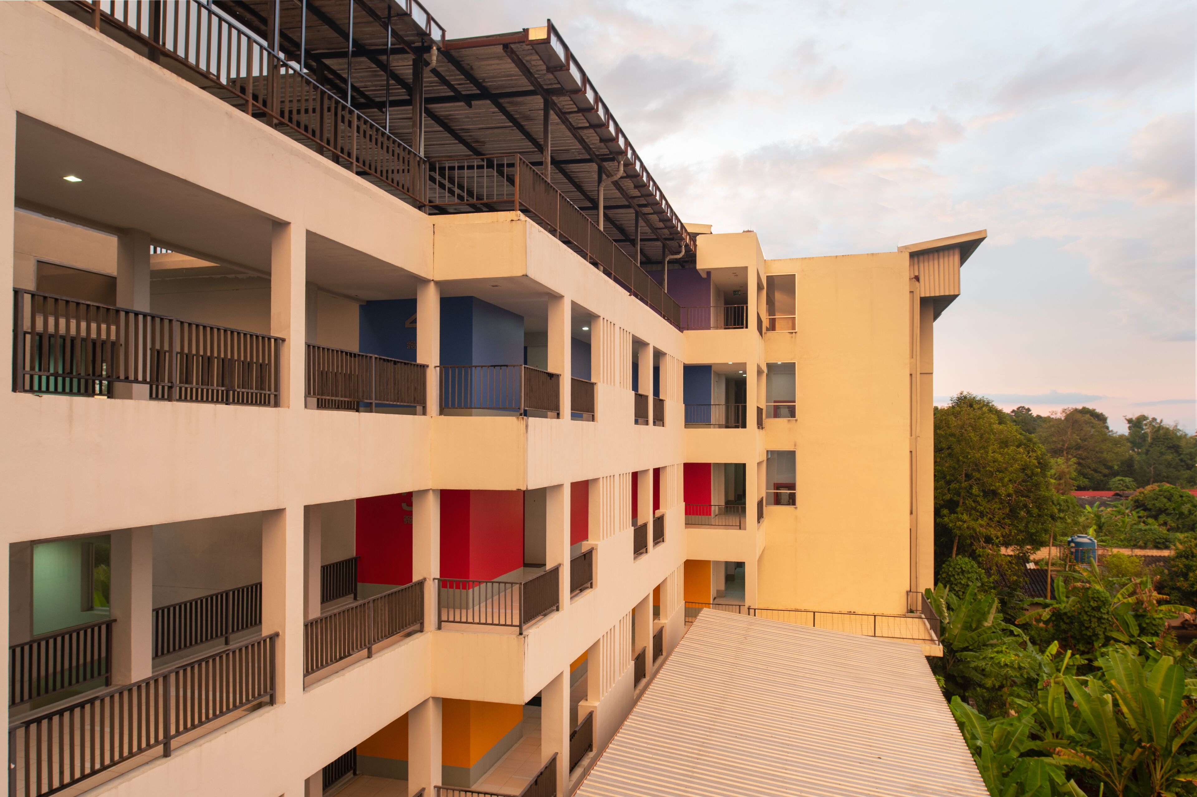 A multi-story hotel with balconies, a flat roof, and a view of greenery.