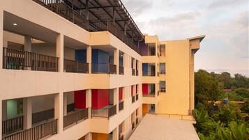 A multi-story hotel with balconies, a flat roof, and a view of greenery.
