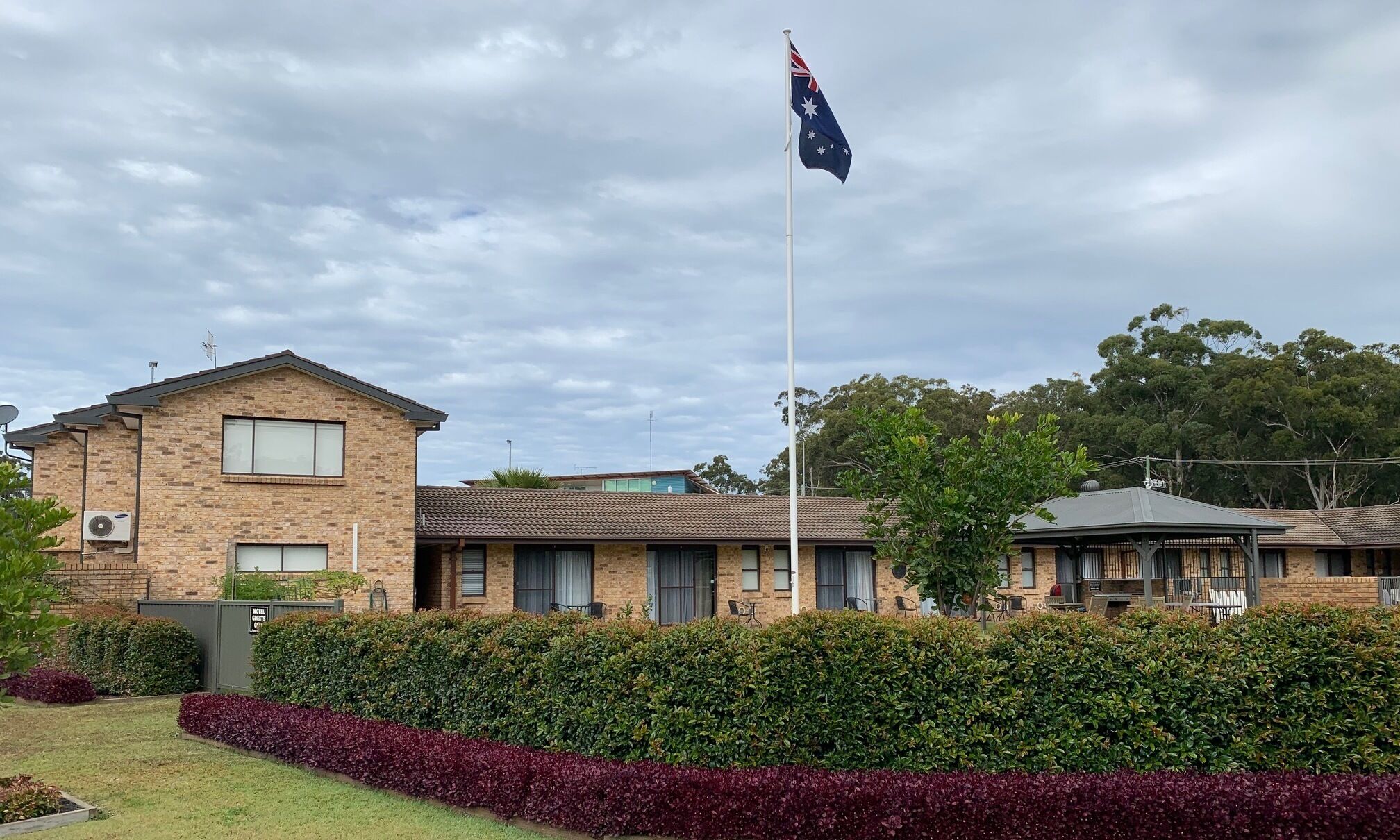 A brick building with a flagpole, a lawn, and a hedge.