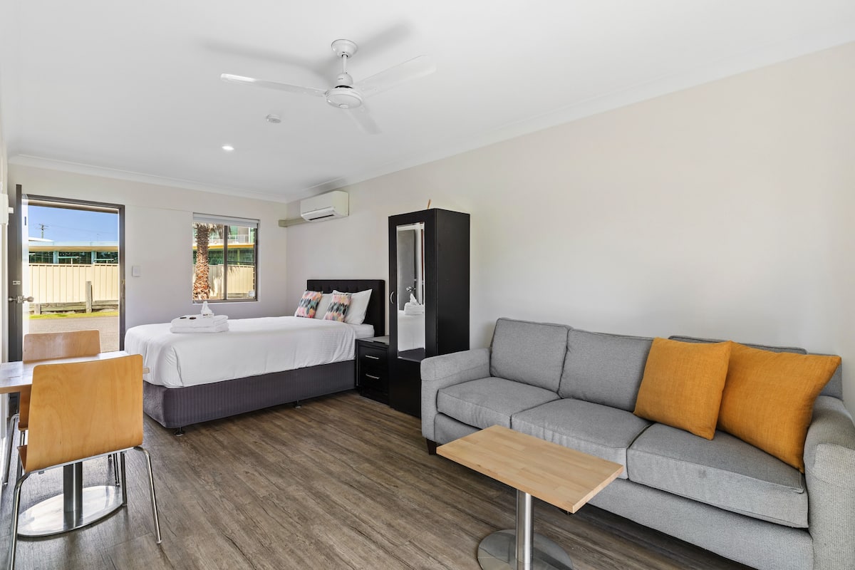 A modern hotel room with a bed, sofa, and a dining area.