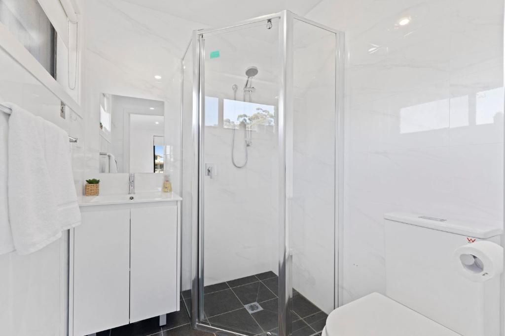 Une salle de bain moderne avec une douche à parois de verre, des meubles blancs et des toilettes.