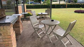 Een terras buiten met een barbecue, tafels en stoelen.