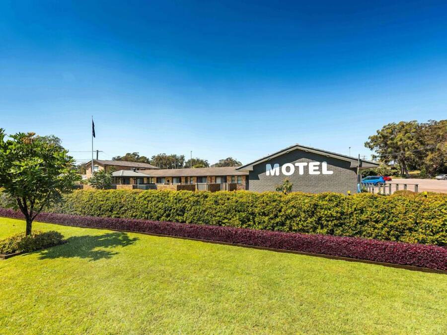 A motel with a prominent "MOTEL" sign, surrounded by well-maintained lawns and hedges.