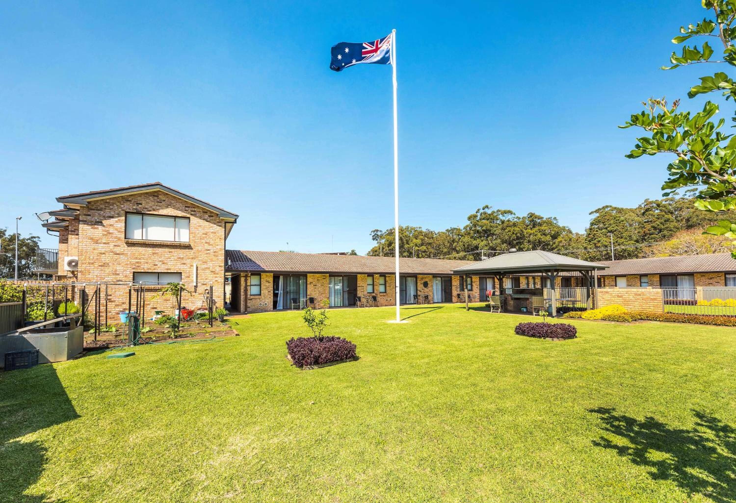 A building with a flagpole, a lawn, and a small garden area.