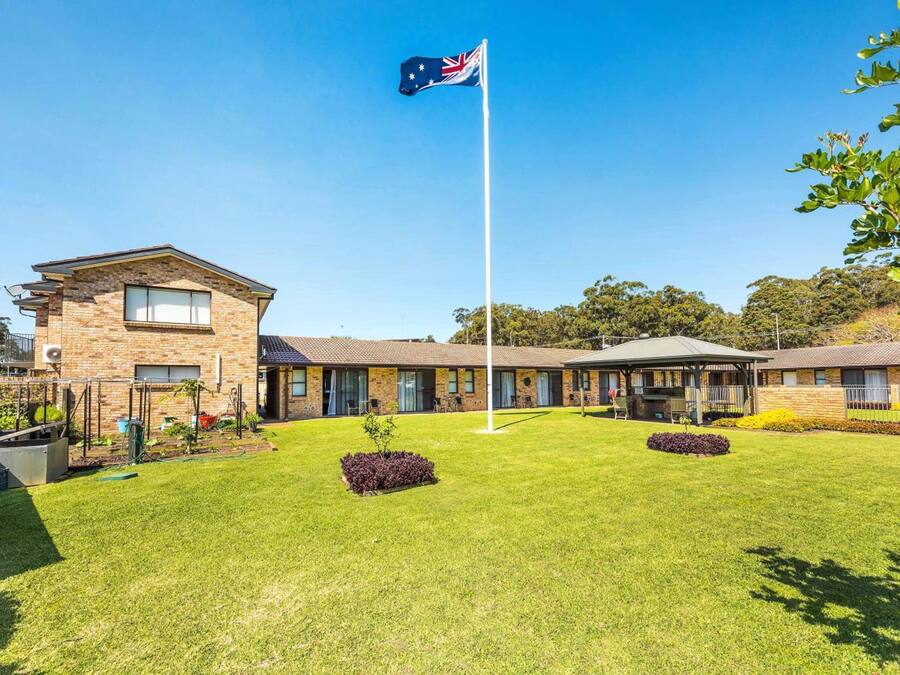 A building with a flagpole, a lawn, and a small garden area.