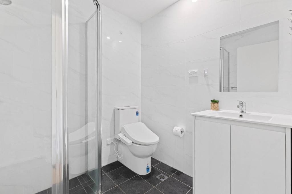 Un baño con cabina de ducha de vidrio, un inodoro, un lavamanos con espejo y una pequeña planta en el mostrador.