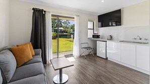 A modern kitchen with white cabinets, a microwave, and a kettle. There is a grey sofa with an orange pillow and a small table. - Lemon Tree Passage Motel (Lemon Tree Passage)