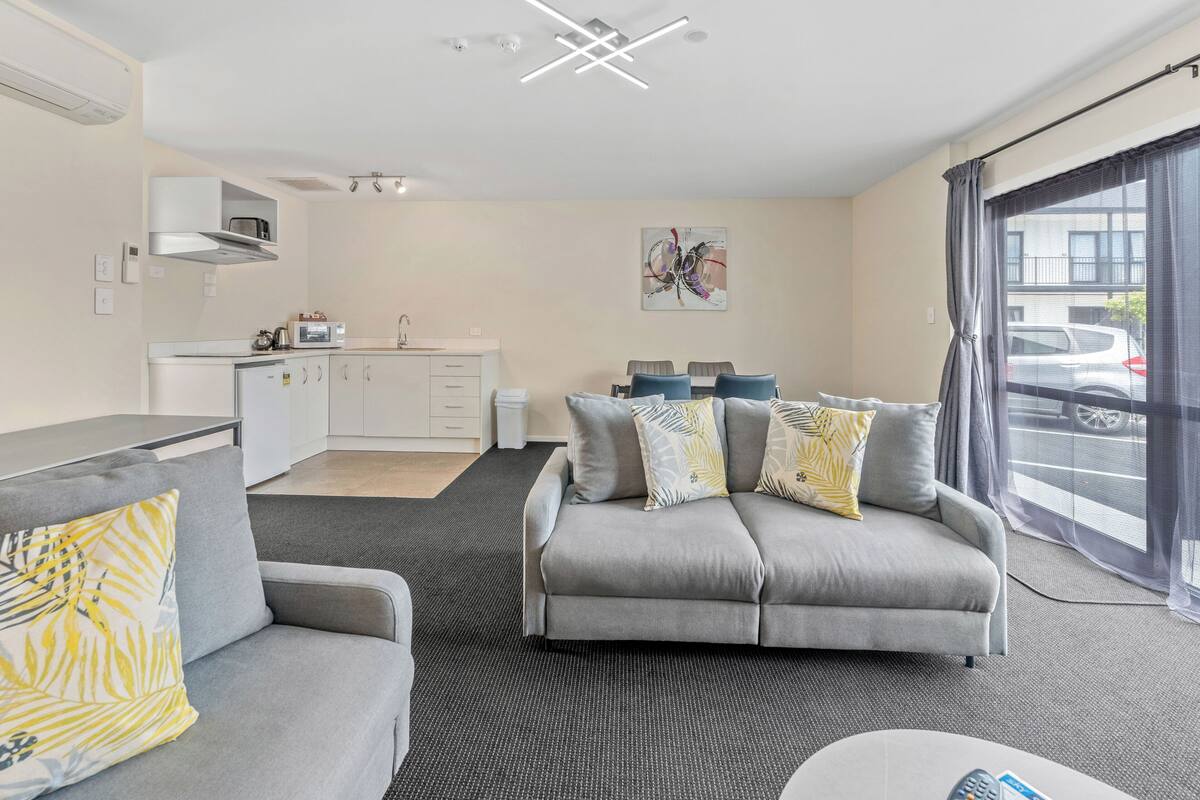 A modern living room with a grey sofa, a grey armchair, and a dining area with a table and chairs.