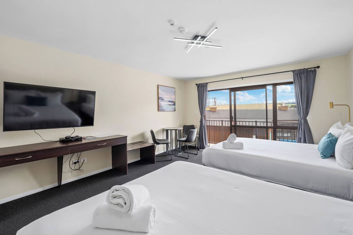 A hotel room with two beds, a desk with a TV, a small table, and chairs.