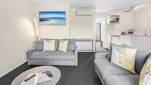 A modern living room with a grey sofa, a coffee table, and a painting of a beach scene. - ASURE Rotorua International Motor Inn (Rotorua)