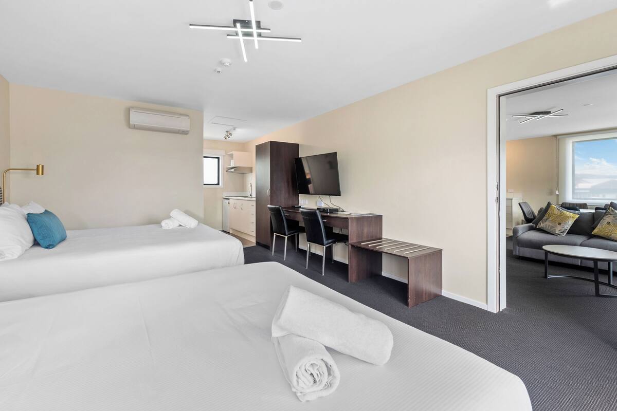A hotel room with two beds, a desk, a TV, and a sofa.