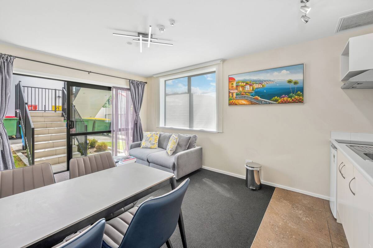 A modern room with a dining table, sofa, and a painting of a coastal scene.