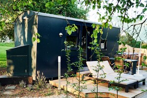 A compact, dark-colored building with a small deck area featuring a single lounge chair and a table.