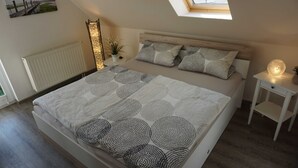 Un dormitorio con tragaluz, cama con ropa de cama estampada, mesita de noche con lámpara y radiador.