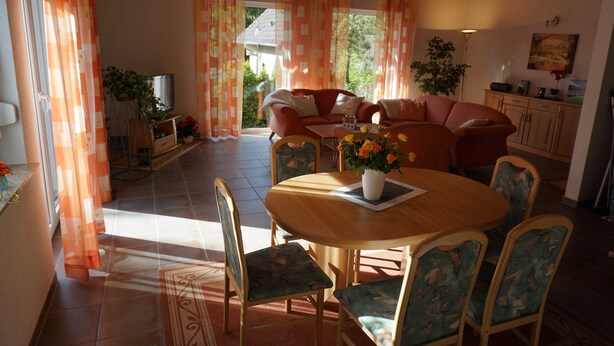 Un comedor con una mesa y sillas de madera, un sofá y cortinas.