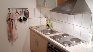 Cocina con estufa a gas, horno y pileta. Hay utensilios colgantes y un escurreplatos.